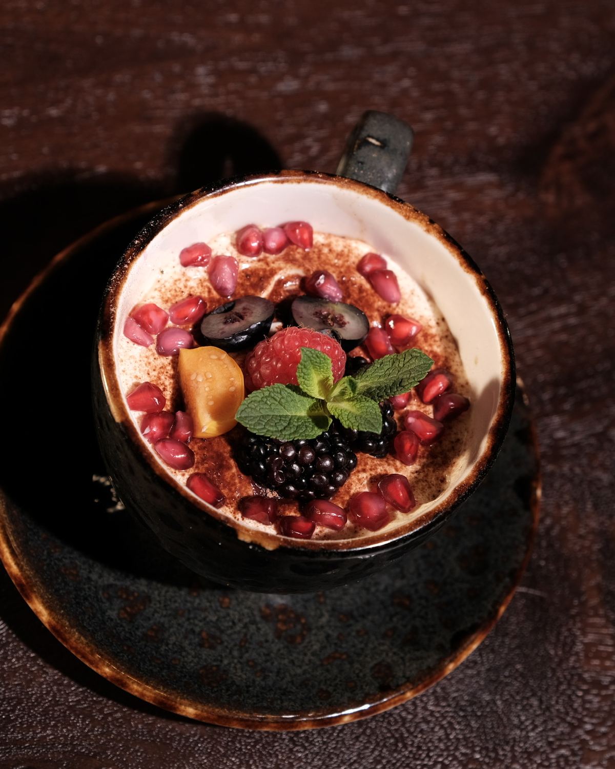 Dessert im Schälchen mit karamellisierter Oberfläche, Brombeeren, Granatapfelkernen und Minze auf dunklem Holz