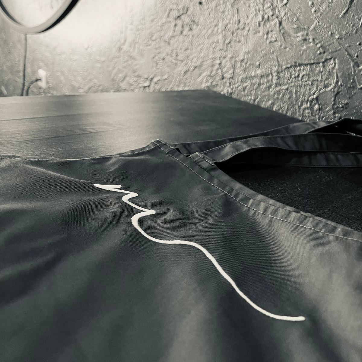 Graue Stoffserviette mit gesticktem weißem Schwung aus dem Marcos-Logo