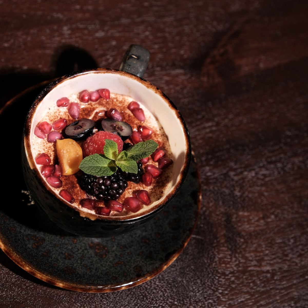 Dessert im Schälchen mit karamellisierter Oberfläche, Brombeeren, Granatapfelkernen und Minze auf dunklem Holz