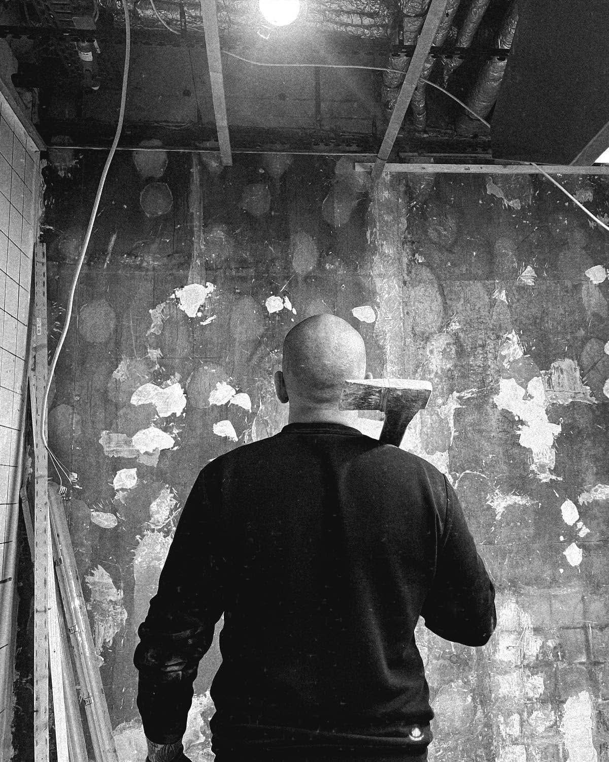 Schwarzweißfoto vom Umbau: ein Mann von hinten vor einer abgeschlagenen Wand, daneben eine Leiter und lose Kabel